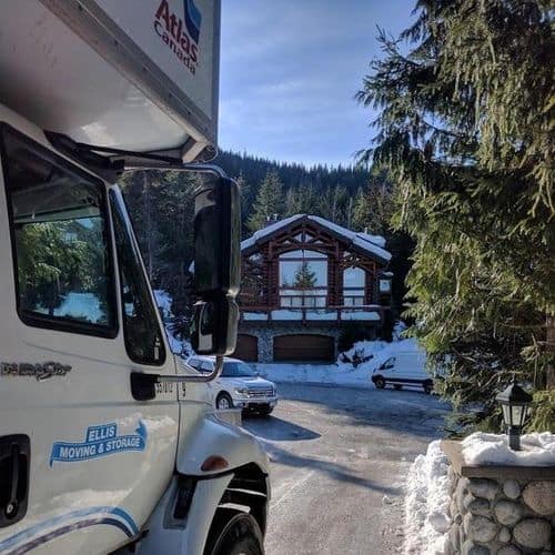 Moving truck near snowy cabin in forest setting.